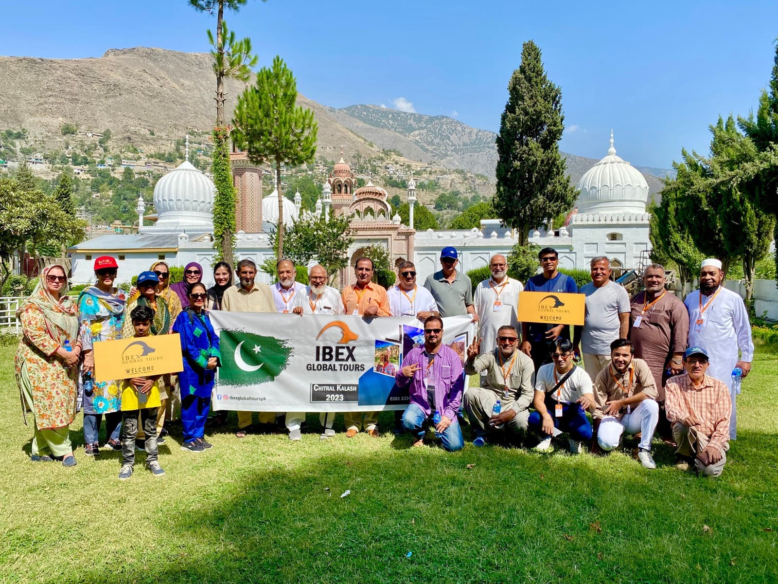 An IBEX group photographed on the lawn in front of the Shahi Masjid in Chitral, holding an IBEX Global Tours banner