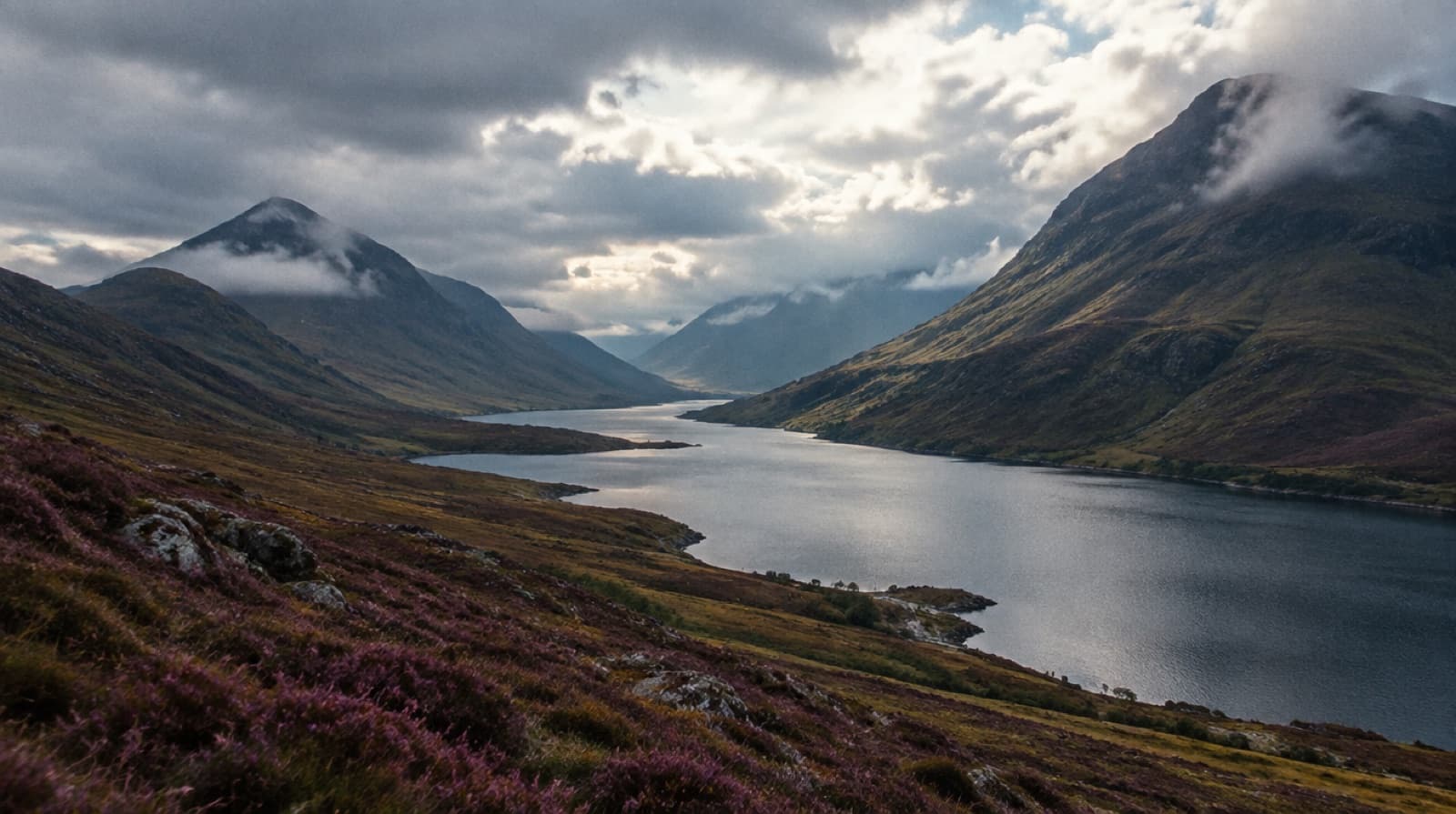 A loch in a long Highland glen under cloud, heather on the slopes