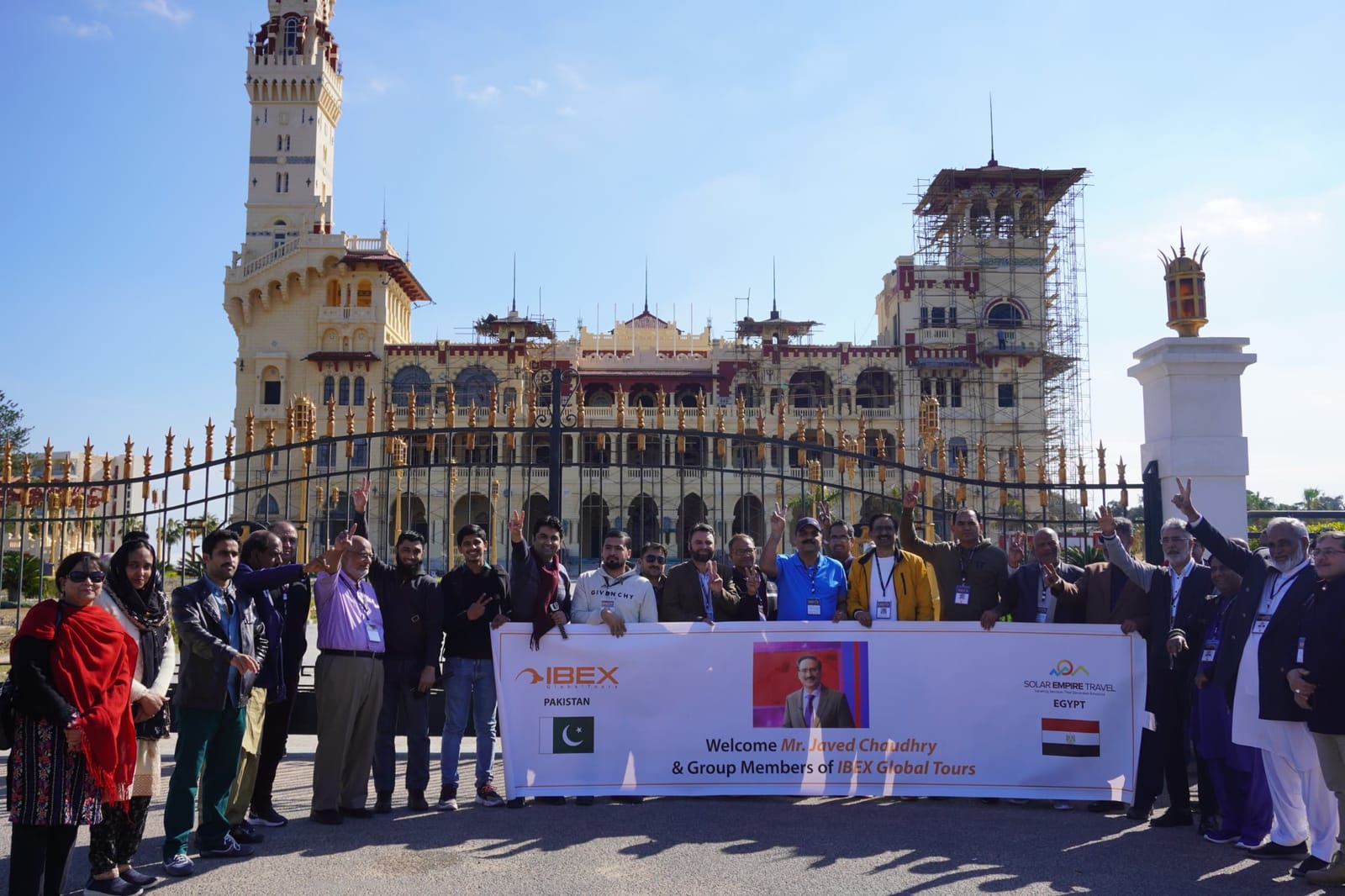 An IBEX group photographed at the gates of the Montaza Palace in Alexandria, holding a welcome banner for IBEX Global Tours